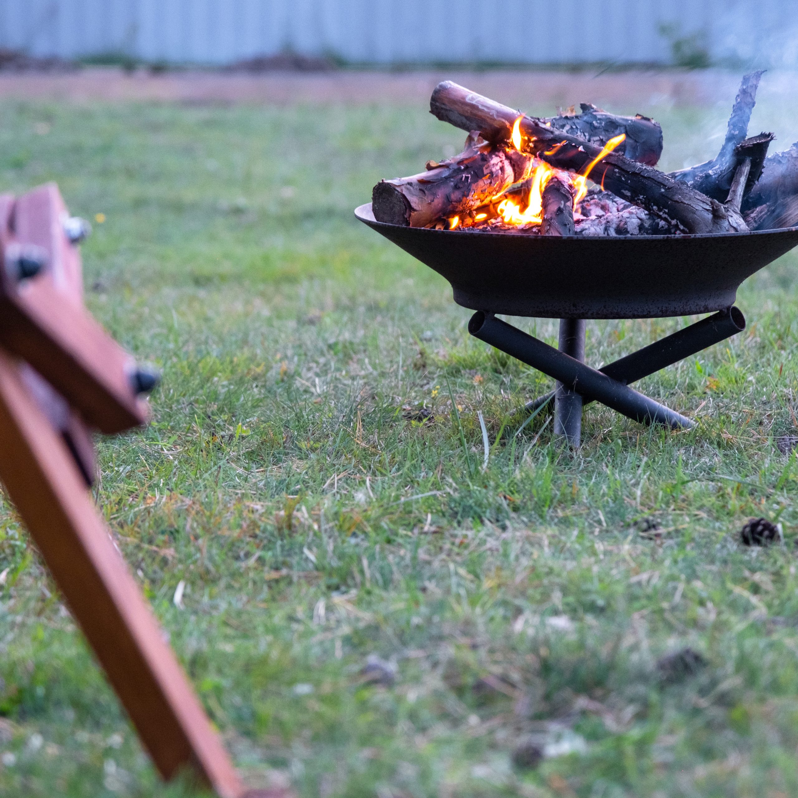 Metal fire bowl with burning wood in the yard and garden rack deck chairs. Safe decorative fire pit, Picnic area in the garden