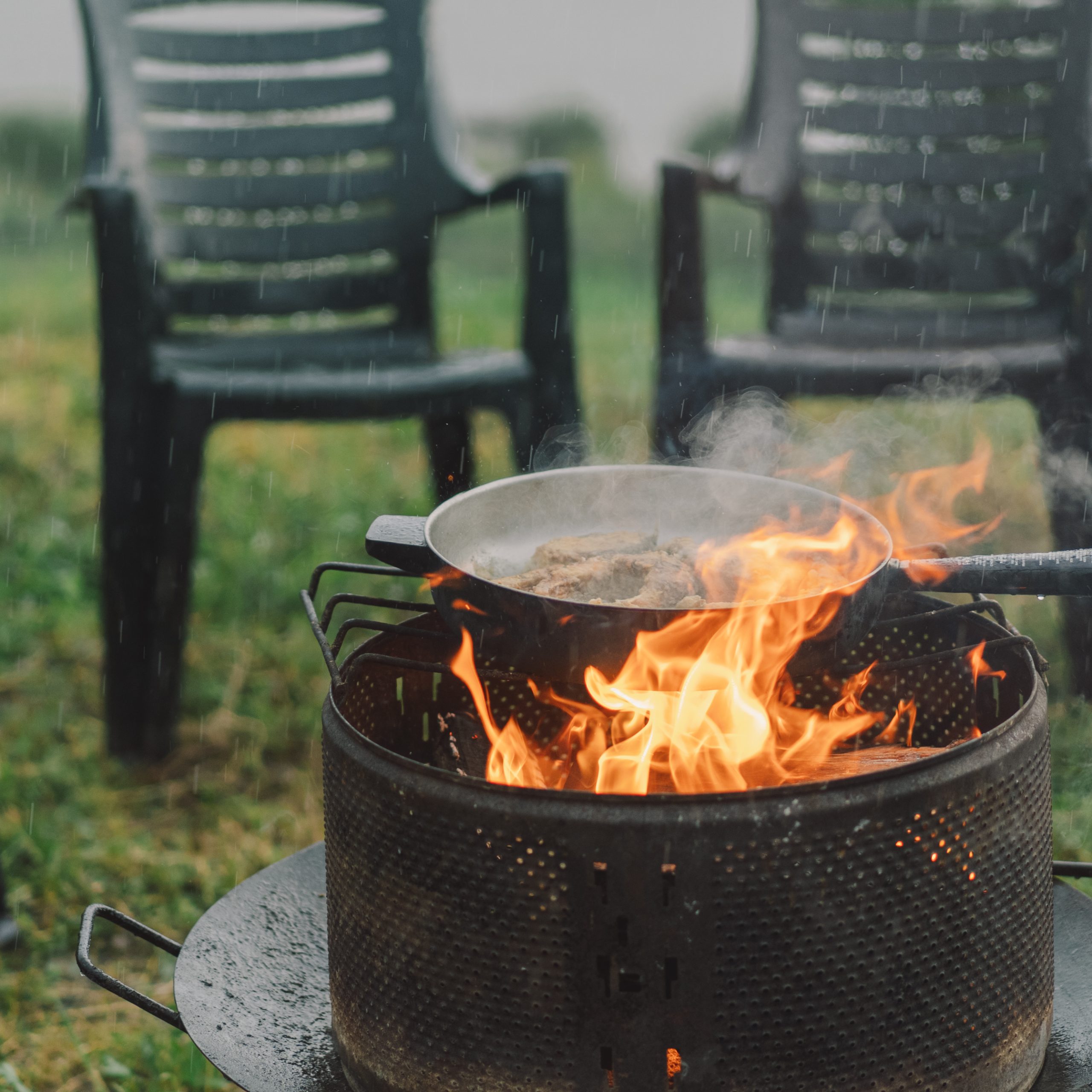 Cooking in the woods outdoors. Man cooking fish on fire in rainy weather, camping outdoors. Tourist on recreation outside. Campsite lifestyle